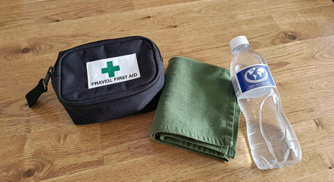 A small travel first aid kit, a water bottle and a folded cloth laid out on a wooden surface.